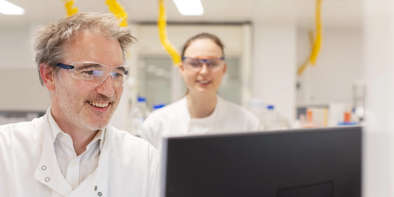 Two scientists smiling and working on a computer