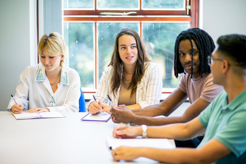 Young people at a table, taking notes and talking to each other