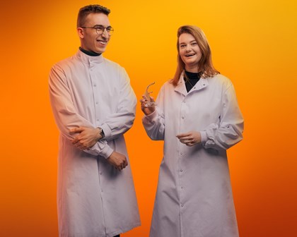 Two employees posing and smiling in front of an orange background