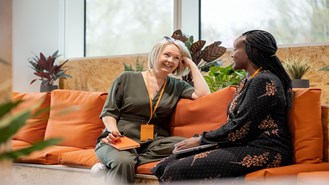 Two female employees sitting on an orange couch talking and laughing together
