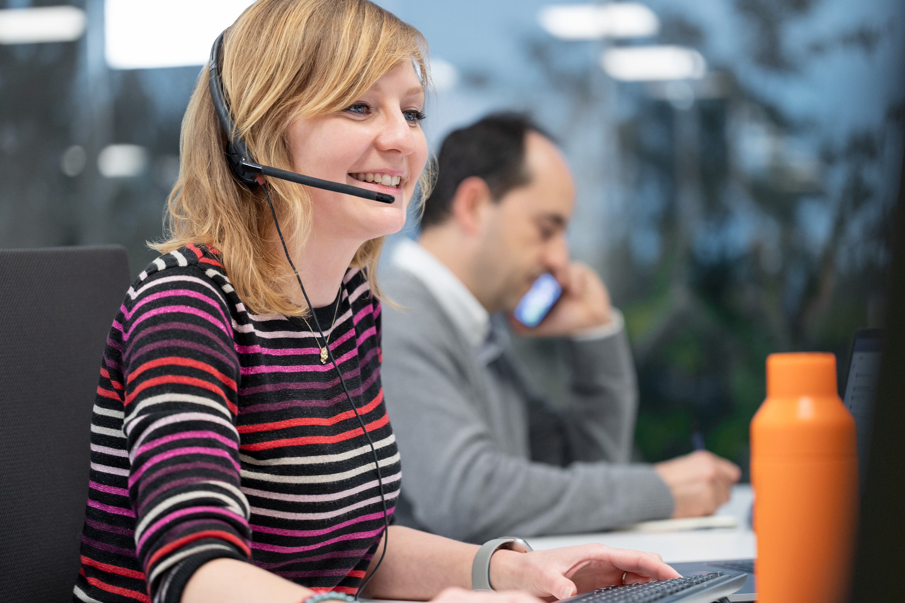 Une femme à son bureau prend des appels grâce à micro-casque filaire