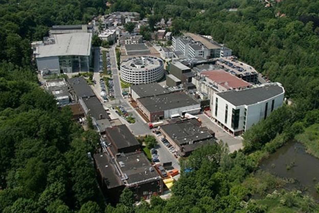 Aerial view of the expansive GSK Biologicals campus in Rixensart, showing research and production facilities integrated into a lush forest landscape.