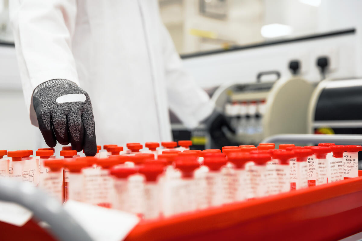 A GSK scientist handles a tray of red-capped vials, illustrating optimized Quality Control operations in Belgium.